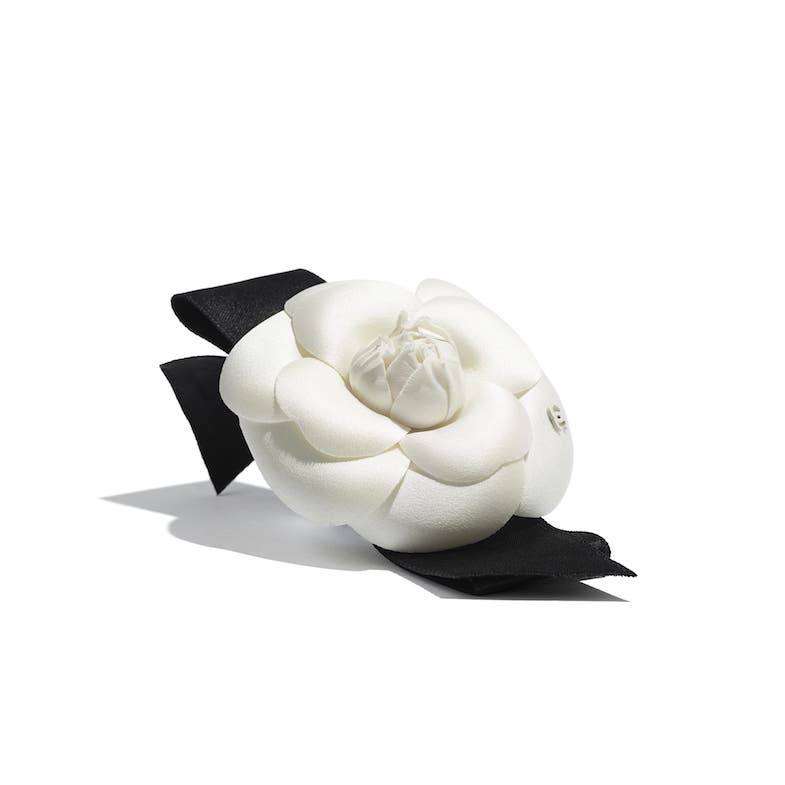 An authentic white leather and silk Chanel camellia flower broach with a black silk ribbon, illustrating one of the core Chanel classic elements.