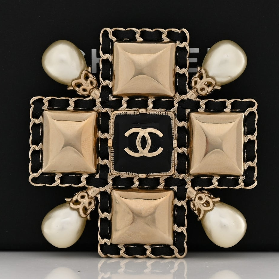 An elaborate Karl Lagerfeld era ornate broach set, featuring geometric gold elements, faux pearls, and a leather-woven chain, combining multiple Chanel classic elements, resting in a black gift box.