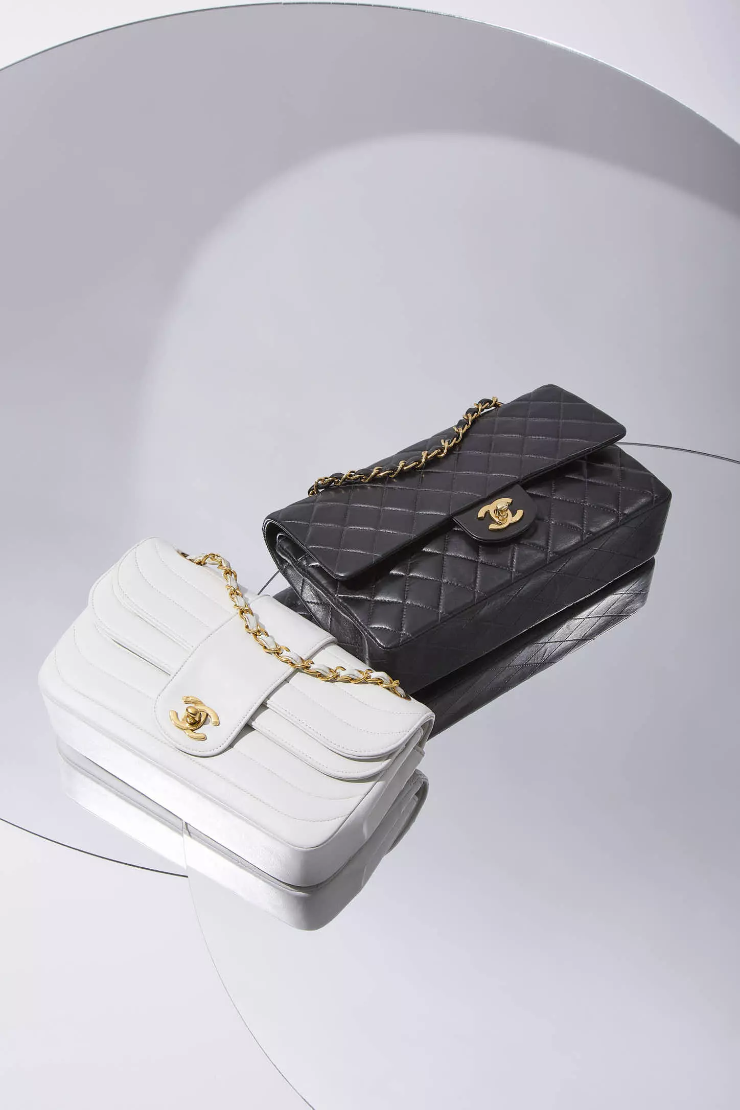 Shop by Brand: White Chanel flap bag laying on top of a black Chanel flap bag.