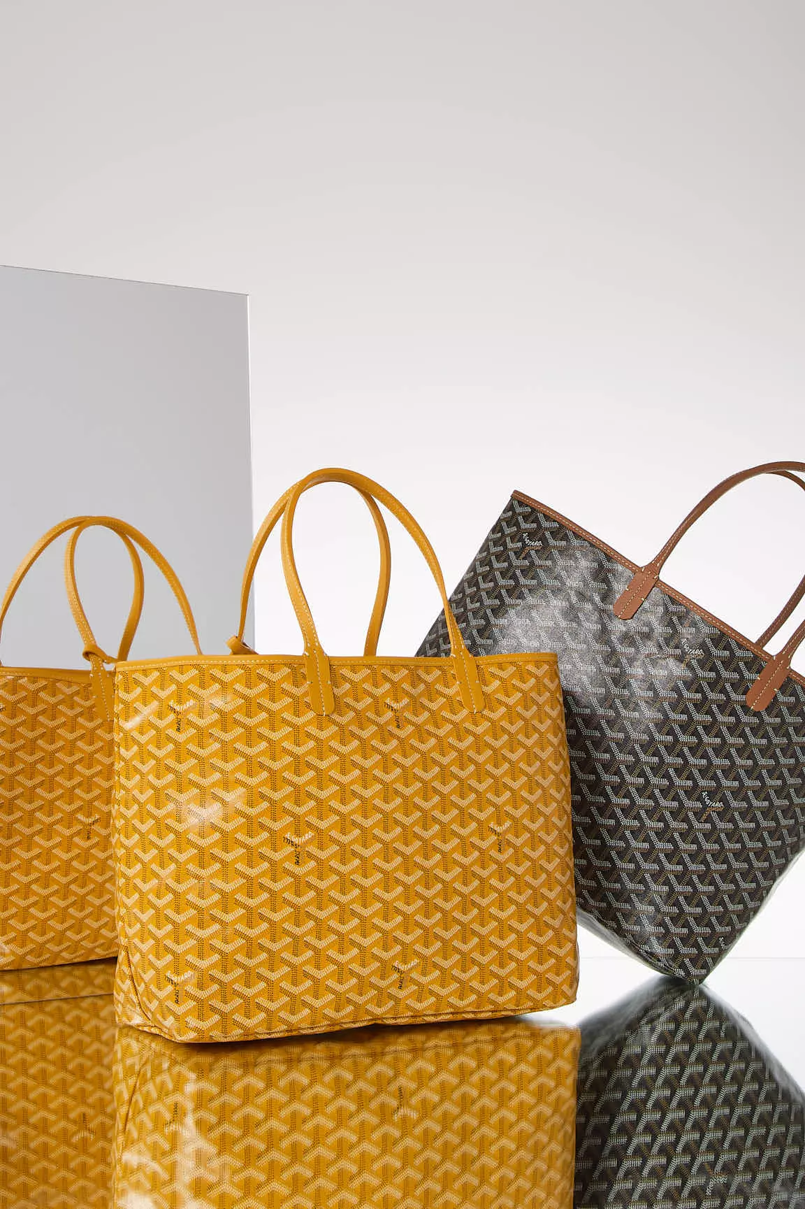 Shop by Brand: Goyard St Louis Yellow Tote and Black Tote on a mirrored surface
