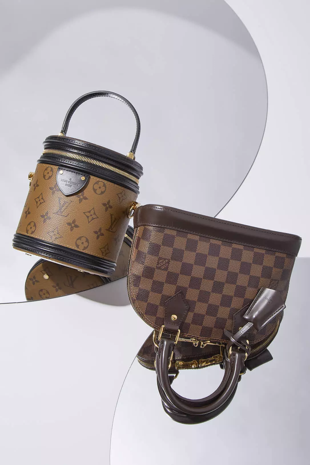 Shop by Brand: Louis Vuitton monogram reverse top handle bag and a Louis Vuitton Damier Ebene Alma BB on a mirrored surface